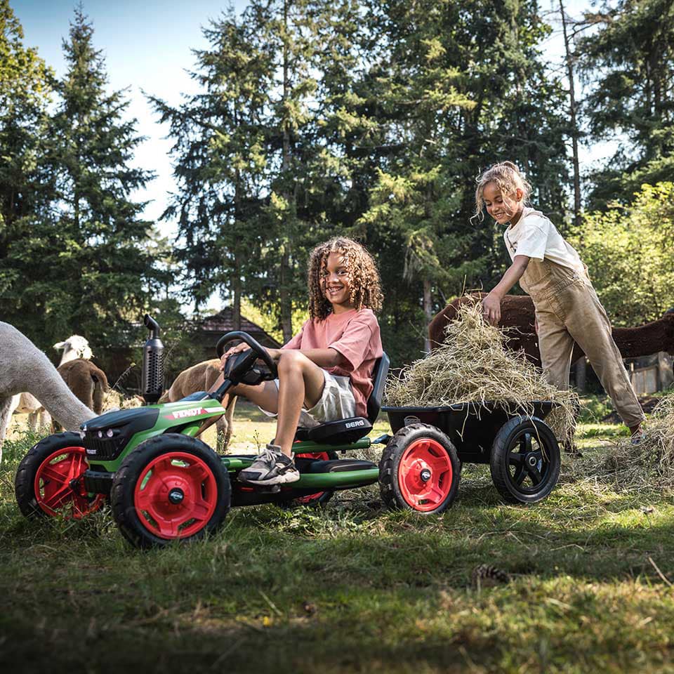 Zwei Mädchen spielen mit dem BERG Buddy Fendt Pedal-Gokart draußen auf dem Bauernhof.