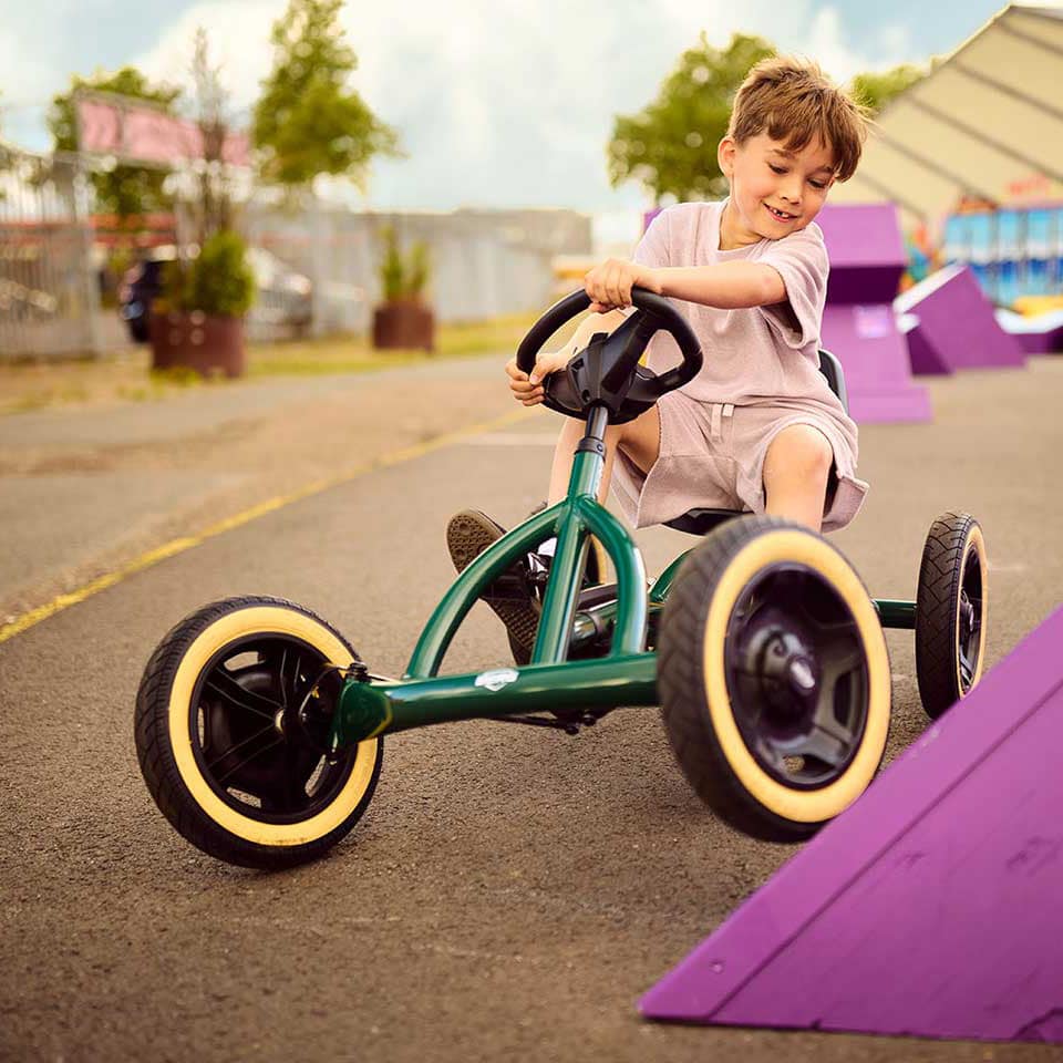 Ein Kind fährt mit dem BERG Buddy Retro Green Pedal-Gokart über ein Hindernis.